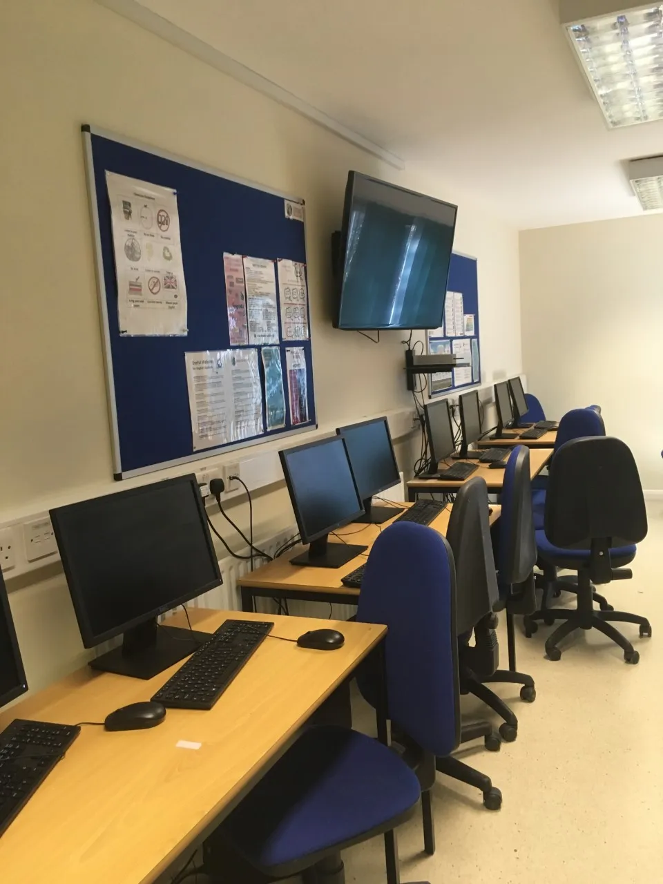 Modern computer lab at Loxdale English Centre Brighton with desktop PCs, blue chairs and interactive display screen
