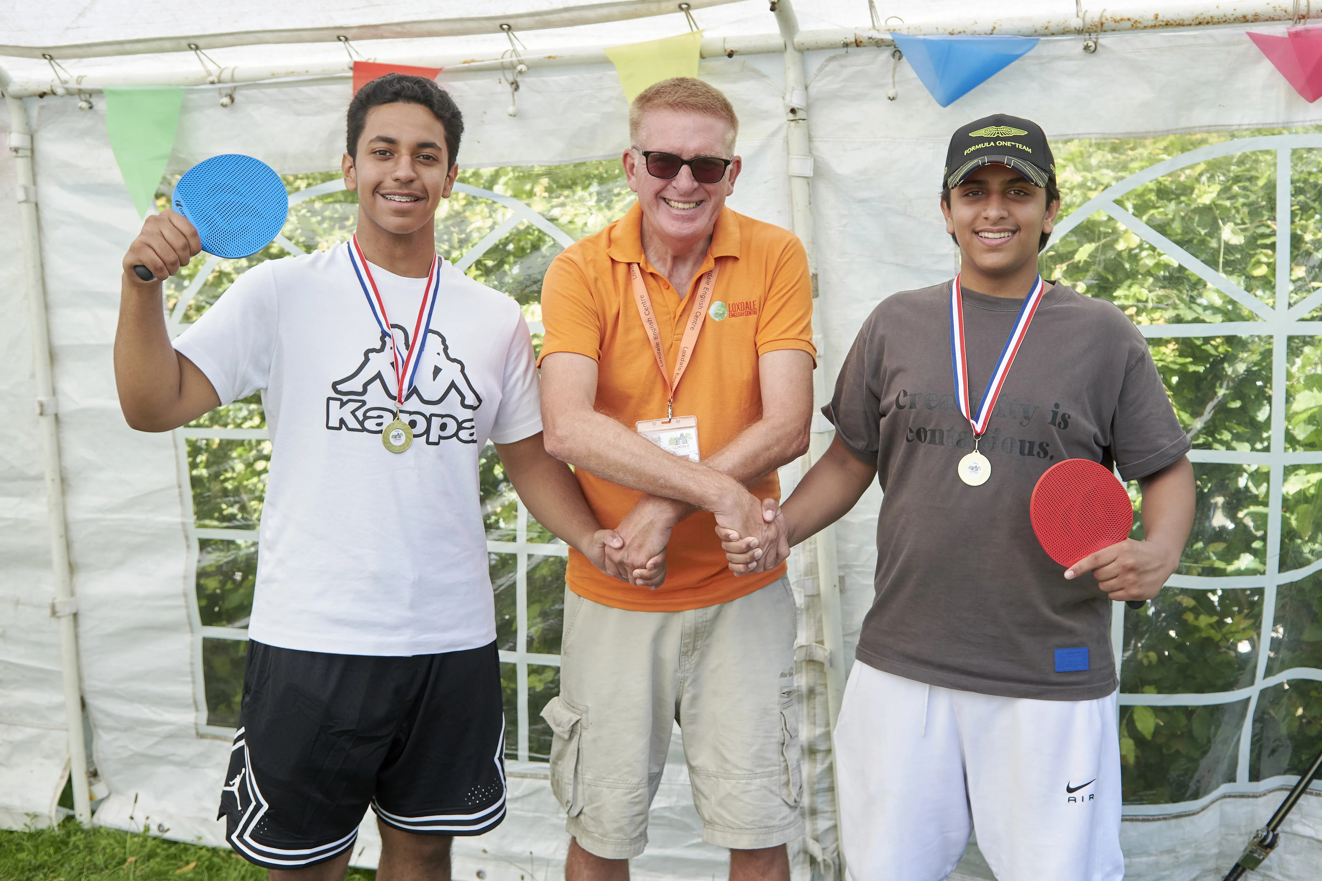 Two young learners with medals and ping pong paddles pose with instructor at Loxdale Brighton summer course