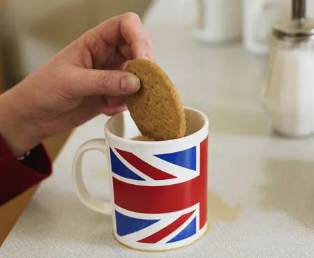 Hand dipping biscuit into tea served in Union Jack mug at Loxdale English Centre Brighton UK